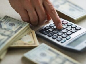 image-close-up-of-mans-hand-using-calculator-and-stacks-of-dollar-bills