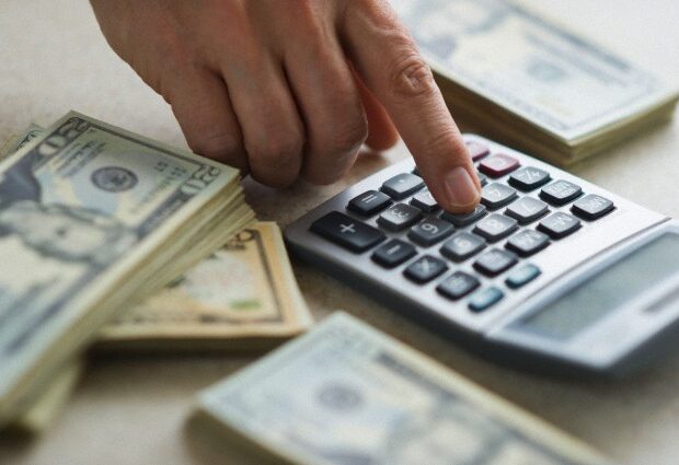 image-close-up-of-mans-hand-using-calculator-and-stacks-of-dollar-bills